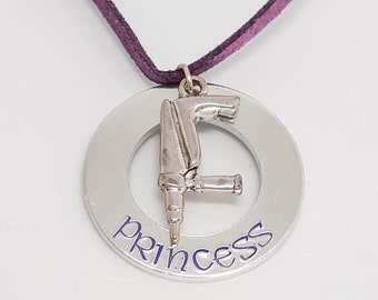 May include: A silver necklace with a purple cord and a round pendant. The pendant has a small silver drill charm and the word "princess" engraved on it.