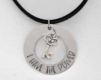 May include: A silver necklace with a black suede cord and a round pendant that says "I have the power" with a small key charm in the center.