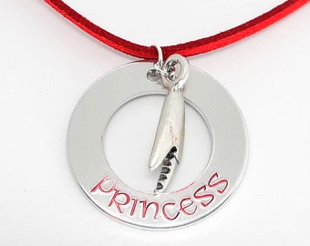 May include: A silver necklace with a red cord and a round pendant that says "princess" with a small silver charm in the center.