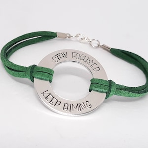May include: Green suede bracelet with a silver circle charm that reads "Stay Focused Keep Aiming".