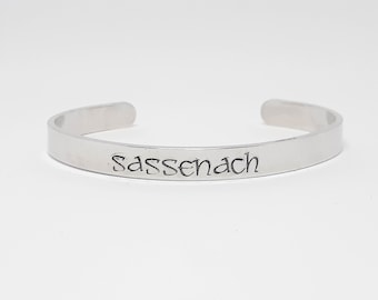 May include: Silver bracelet with the word "Sassenach" engraved on it.