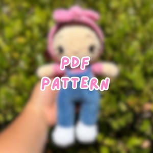 May include: A handmade doll wearing blue dungarees, a pink shirt, and a pink headband. The doll has white shoes and a light skin tone. The words "PDF PATTERN" are written across the doll in pink letters.