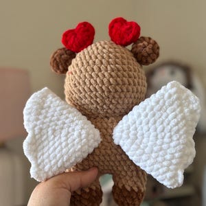 Puede incluir: Un juguete de peluche de color marr&oacute;n tejido a crochet con alas blancas y corazones rojos en la cabeza. El juguete est&aacute; hecho de hilo suave y tiene una expresi&oacute;n dulce y caprichosa.