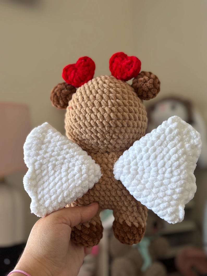 Puede incluir: Un juguete de peluche de color marr&oacute;n tejido a crochet con alas blancas y corazones rojos en la cabeza. El juguete est&aacute; hecho de hilo suave y tiene una expresi&oacute;n dulce y caprichosa.