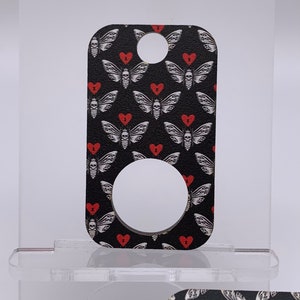 May include: Black and white key chain with a repeating pattern of red hearts and a moth with a skull and crossbones. The key chain has a round hole in the center.