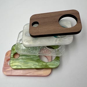 May include: A stack of five rectangular keychains with different patterns and colors. The top keychain is made of dark wood and has a circular hole in the center. The other keychains are made of a translucent material with a variety of patterns, including glitter, swirls, and a green marbled design.