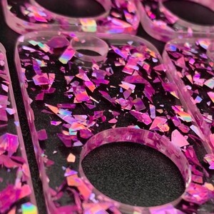 May include: A set of pink keychains with a round hole in the centre. The keychains are made of clear resin with iridescent glitter embedded in the resin.