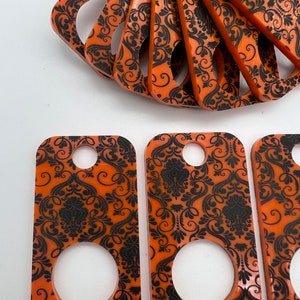 May include: Set of eight orange and black keychains with a damask pattern. Each keychain has a round hole in the center.