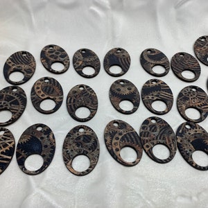 May include: Twenty oval-shaped wooden charms with a steampunk design featuring intricate gears and cogs in shades of brown and black.