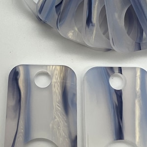 May include: Two white and blue marbled keychains with a hole at the top and a large circle cut out in the middle.