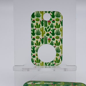 May include: A green and white key chain with a cactus pattern. The key chain has a round hole in the center.