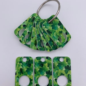 May include: A set of seven green shamrock patterned keychains with a silver ring. Three of the keychains are separate and the other four are attached to the ring.