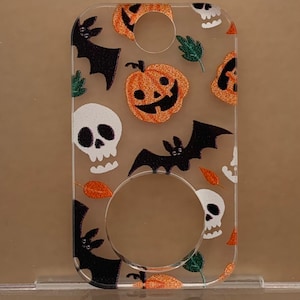 May include: A clear acrylic keychain with a Halloween theme. The keychain features a repeating pattern of orange pumpkins with jack-o'-lantern faces, black bats, and white skulls.
