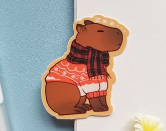 May include: A brown capybara wearing a red and white sweater with a black and red plaid scarf. The capybara is sleeping and has the text "zzz" above it.