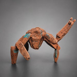 May include: An abstract sculpture in reddish-brown, crafted to resemble an insect or creature. The textured surface features touches of blue paint. The sculpture's limbs are extended, giving it a dynamic pose.