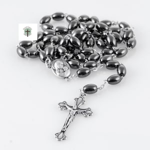 May include: A rosary with dark gray oval beads and a silver crucifix. The rosary features a silver centerpiece with an image of Mary and baby Jesus. The beads are strung on a silver chain.
