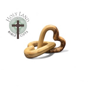 May include: A wooden heart-shaped sculpture with interlocking loops. The sculpture is made of light-colored wood with visible grain patterns. The logo for Holy Land Bible Gifts is in the upper left corner.