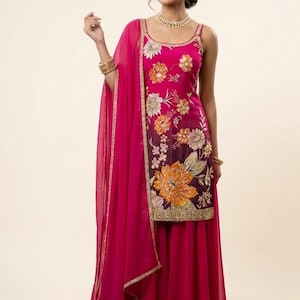 May include: A vibrant fuchsia-colored ensemble featuring a floral embroidered top and wide-leg pants. The top has a scoop neckline and spaghetti straps. A matching sheer scarf is draped over the shoulder. Gold trim accents the outfit.