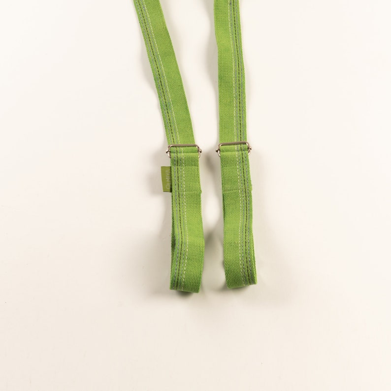 May include: Two green fabric straps with silver metal buckles. The straps are sewn with white thread.