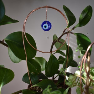May include: A potted plant with green leaves and a copper wire hoop with a blue evil eye charm hanging from it.