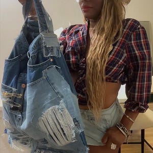 Puede incluir: Un bolso tote de mezclilla con detalles desgastados, sostenido. El bolso est&aacute; hecho de jeans reciclados, con bolsillos, rasgaduras y alfileres de seguridad. Un sombrero de vaquero de mezclilla y una camisa a cuadros completan el look.
