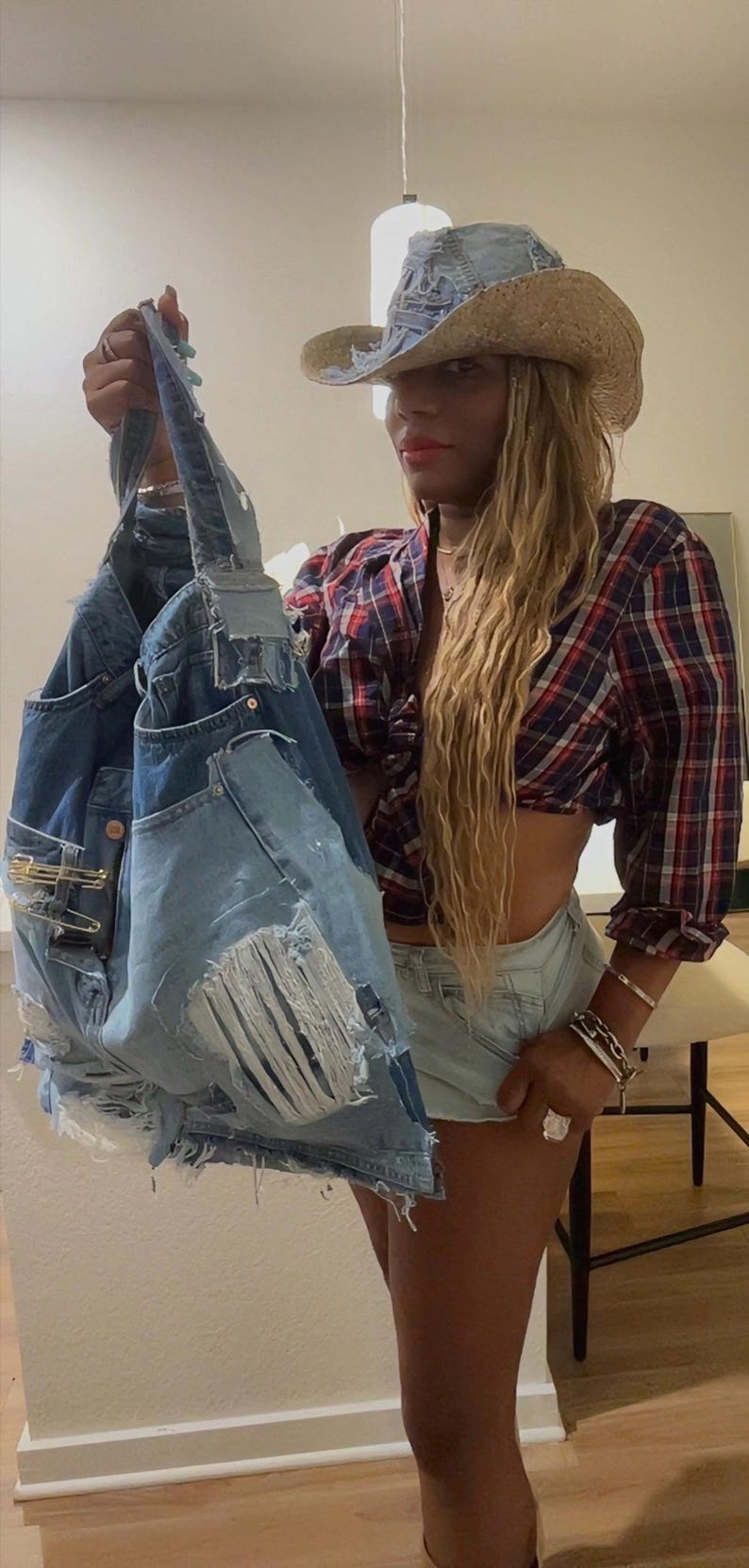 Puede incluir: Un bolso tote de mezclilla con detalles desgastados, sostenido. El bolso est&aacute; hecho de jeans reciclados, con bolsillos, rasgaduras y alfileres de seguridad. Un sombrero de vaquero de mezclilla y una camisa a cuadros completan el look.