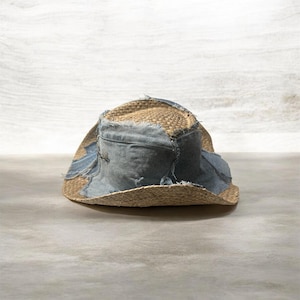Puede incluir: Un sombrero de paja desgastado con parches de mezclilla. El sombrero presenta un tejido de paja natural con detalles de mezclilla azul claro alrededor de la corona y el ala. La mezclilla tiene un aspecto desgastado y deshilachado, lo que a&ntilde;ade al estilo vintage &uacute;nico del sombrero.