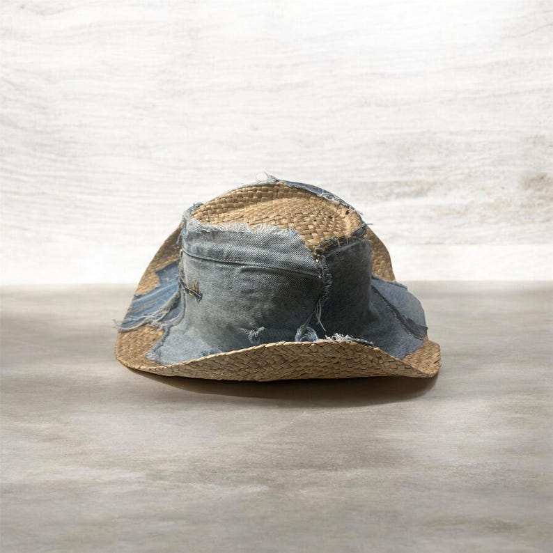 Puede incluir: Un sombrero de paja desgastado con parches de mezclilla. El sombrero presenta un tejido de paja natural con detalles de mezclilla azul claro alrededor de la corona y el ala. La mezclilla tiene un aspecto desgastado y deshilachado, lo que a&ntilde;ade al estilo vintage &uacute;nico del sombrero.