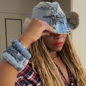 Puede incluir: Un sombrero de vaquero de mezclilla azul claro con un dise&ntilde;o desgastado y un ala de paja tejida. El sombrero se combina con una pulsera de mezclilla a juego. La persona lleva una camisa a cuadros roja, blanca y azul.