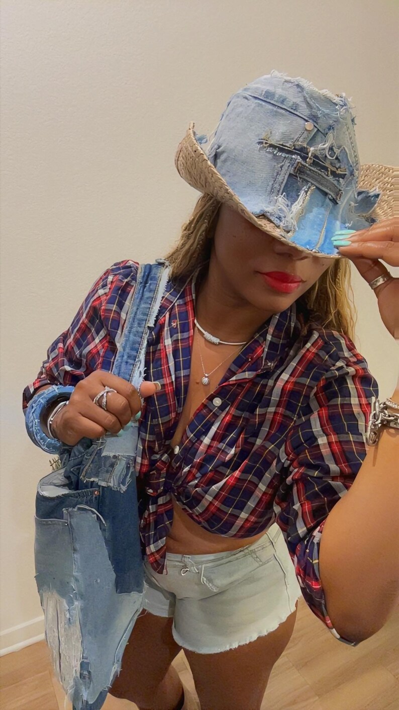 Puede incluir: Un sombrero de mezclilla y paja con detalles desgastados. El sombrero se combina con una camisa a cuadros roja, azul y blanca, un bolso tote de mezclilla y pantalones cortos de mezclilla azul claro. El atuendo se complementa con joyas de plata.