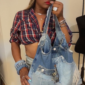 Puede incluir: Un bolso tote de mezclilla con un dise&ntilde;o de retazos, con bolsillos y detalles desgastados. El bolso se combina con un sombrero de vaquero de mezclilla a juego. El atuendo incluye una camisa a cuadros roja y azul.