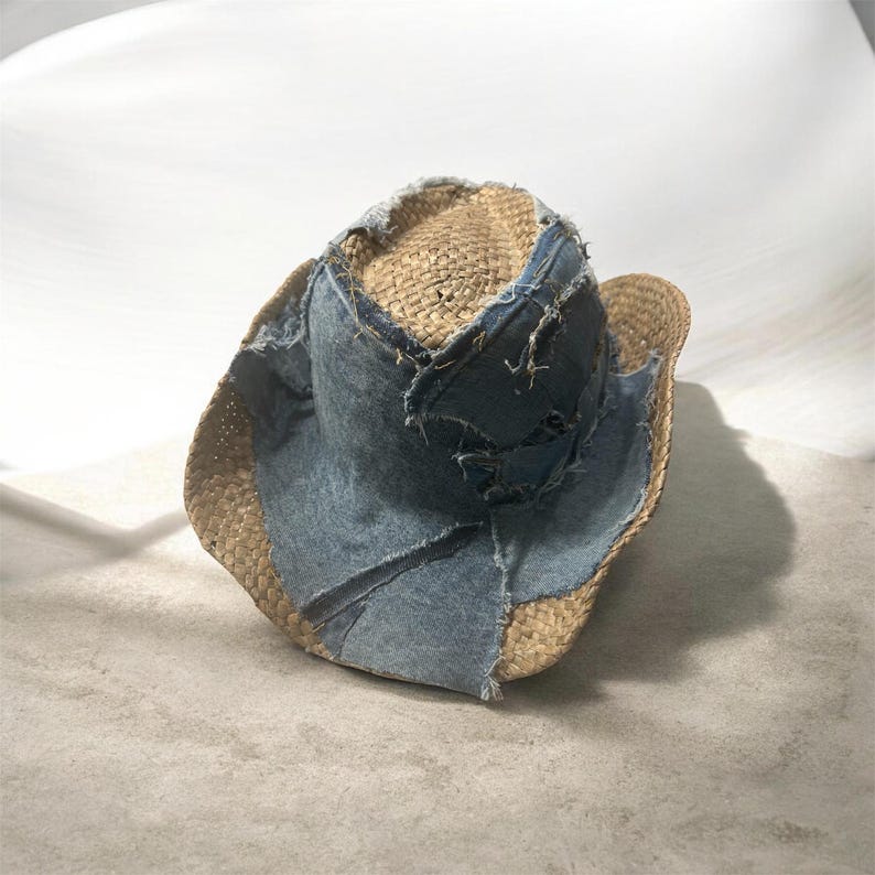 Puede incluir: Un sombrero de vaquero de paja con un dise&ntilde;o de patchwork de mezclilla. El sombrero presenta un color paja natural con parches de mezclilla azul claro cosidos en la corona y el ala. La mezclilla tiene un borde deshilachado y desgastado.