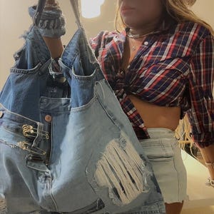 Puede incluir: Un bolso tote de mezclilla azul claro con detalles desgastados, levantado. El bolso est&aacute; hecho de mezclilla reciclada, con secciones rasgadas y herrajes met&aacute;licos. El dise&ntilde;o del bolso es informal y elegante, adecuado para el uso diario.