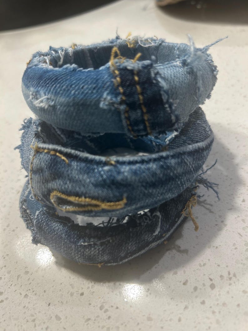Puede incluir: Tres pulseras de mezclilla apiladas. Cada pulsera est&aacute; hecha de tela de mezclilla azul con bordes deshilachados y costuras amarillas. Las pulseras est&aacute;n apiladas, creando un efecto en capas.