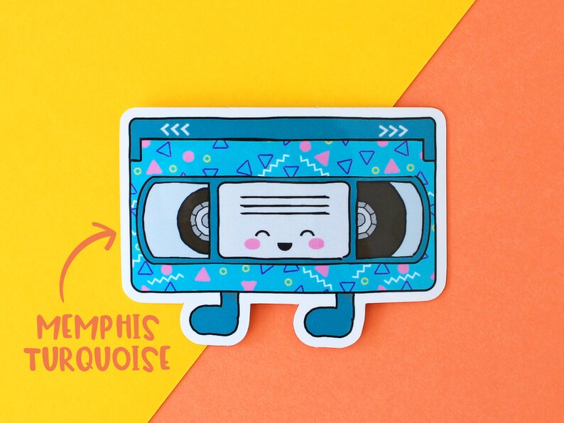 May include: A blue and turquoise VHS tape sticker with a happy face and a geometric pattern. The sticker says "<< >>" on the top and "Memphis Turquoise" on the bottom.