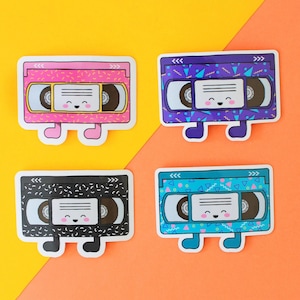 May include: Four colorful cassette tape stickers with a retro 90s design. Each sticker has a smiling face and a different color background: pink, purple, black, and blue.