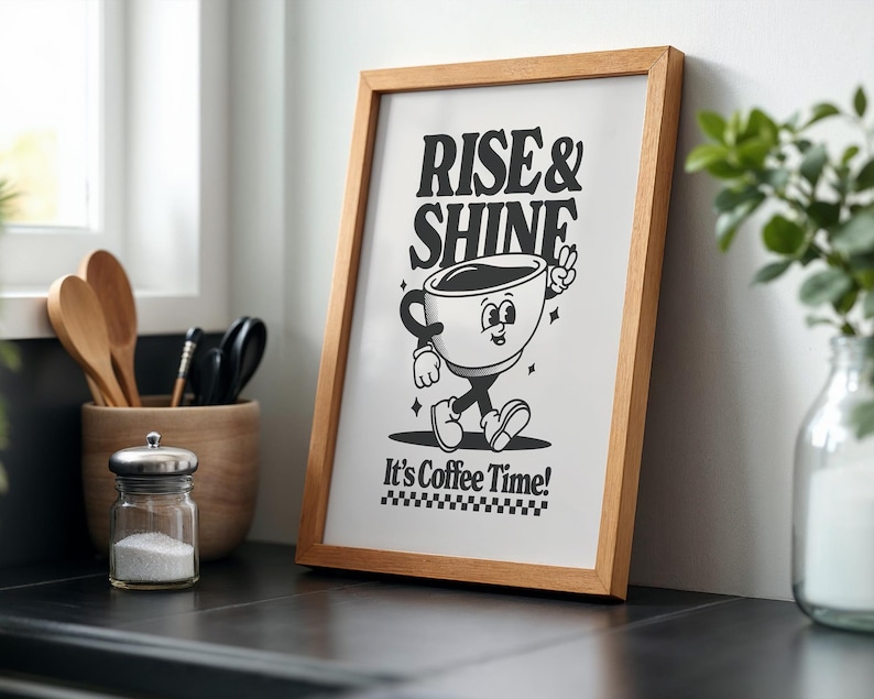 May include: A framed print with a black and white illustration of a coffee cup with legs and arms. The text "Rise & Shine" is above the cup and "It's Coffee Time!" is below the cup.