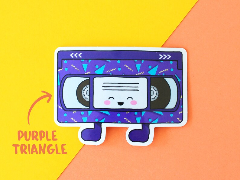 May include: A purple and blue VHS tape with a happy face and a 90s style geometric pattern. The tape has the words "<<<" and ">>>" on the top.