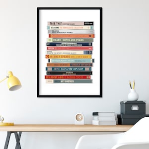 May include: A framed print of a stack of cassette tapes with the titles of popular albums from the 1990s and 2000s. The titles include "Take That", "Madonna", "The Invisible Band", "Keane", "Britney Spears", "The Verve", "Blink 182", and "Avicii".