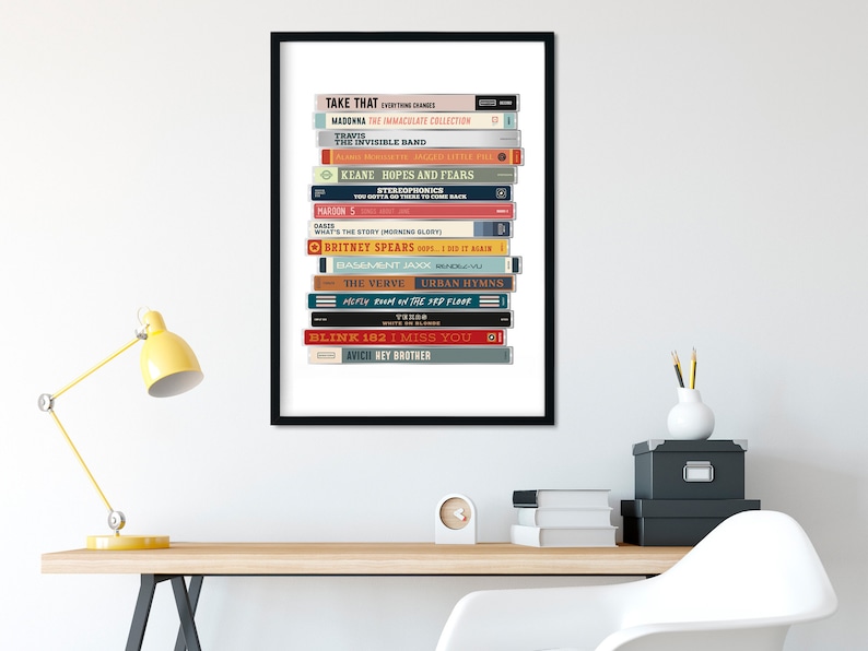 May include: A framed print of a stack of cassette tapes with the titles of popular albums from the 1990s and 2000s. The titles include "Take That", "Madonna", "The Invisible Band", "Keane", "Britney Spears", "The Verve", "Blink 182", and "Avicii".