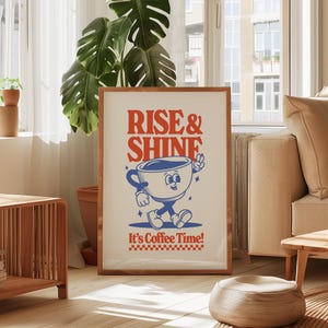 May include: A framed poster with a cartoon coffee cup character. The poster has the text "Rise & Shine" in red and "It's Coffee Time!" in blue. The coffee cup is blue and white and has a smiling face. The background of the poster is white.