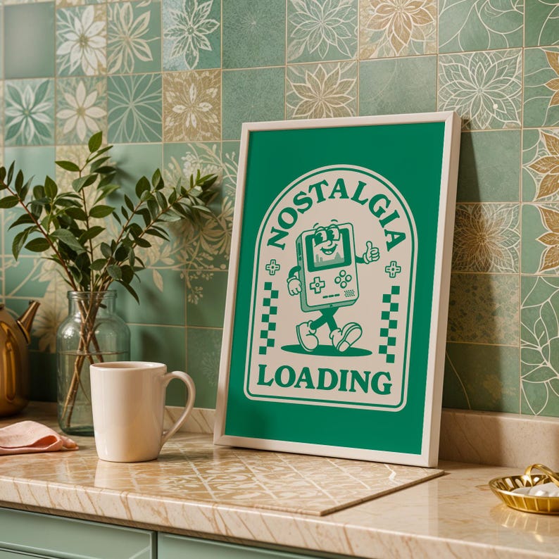 May include: A framed green poster with the word "NOSTALGIA" in a circular design, featuring a cartoon game console giving a thumbs up. The word "LOADING" is below the console. The poster is in a white frame.