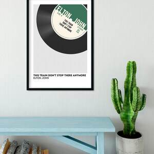 May include: A black and white framed print of a vintage record with the text "ELTON JOHN" and "THIS TRAIN DON'T STOP THERE ANYMORE" on a white background.