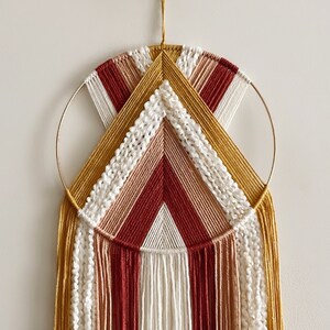 May include: A macrame wall hanging with a circular wooden frame and long, colourful tassels in shades of red, white, and yellow.