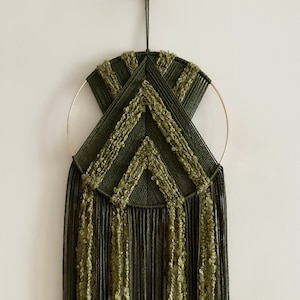 May include: A green and gold macrame wall hanging with a geometric design. The hanging features a circular hoop with fringe tassels.