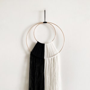 May include: A black and white yarn wall hanging with fringe, woven through two gold metal hoops.