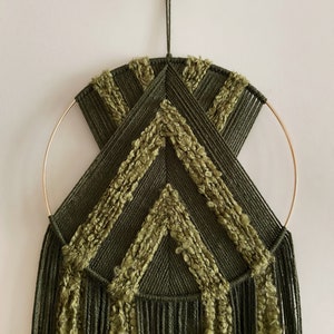 May include: A green and gold macrame wall hanging with a geometric design. The hanging features a circular hoop and long fringe.