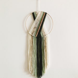 May include: A green and white macrame wall hanging with wooden beads and a gold hoop.