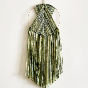 May include: A green and white macrame wall hanging with a circular wooden frame and long fringe.