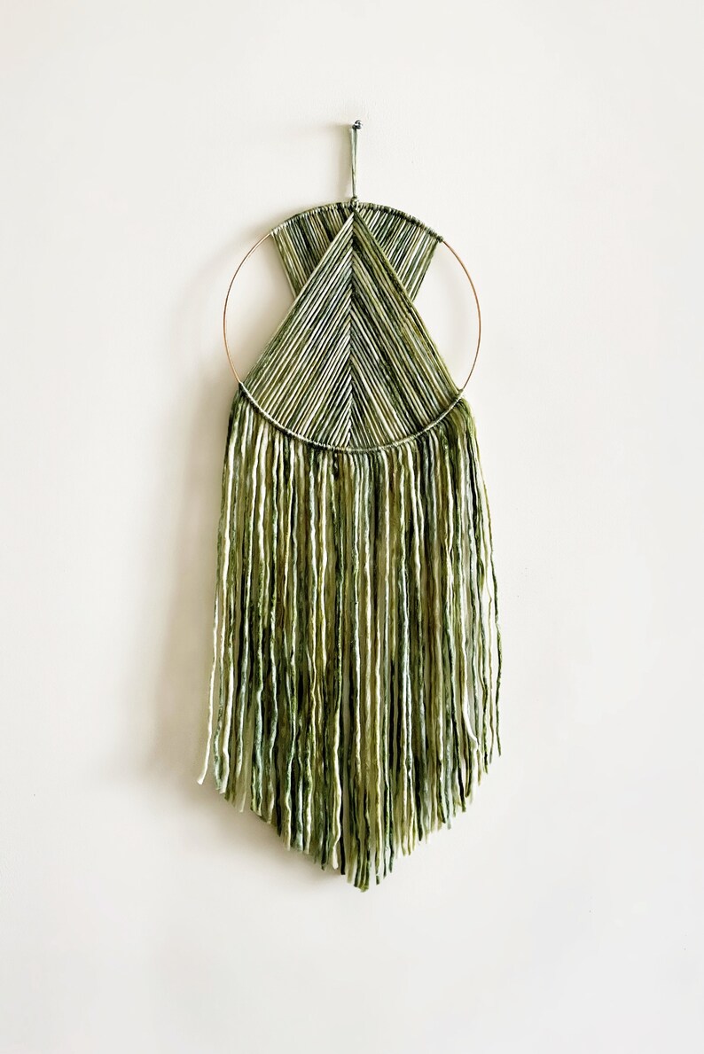 May include: A green and white macrame wall hanging with a circular wooden frame and long fringe.